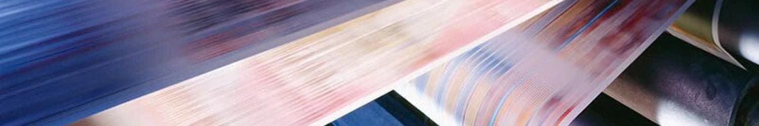 Close-up of a fast-moving printing press with colorful pages being printed in a blur, showing the speed and mechanics of the printing process.