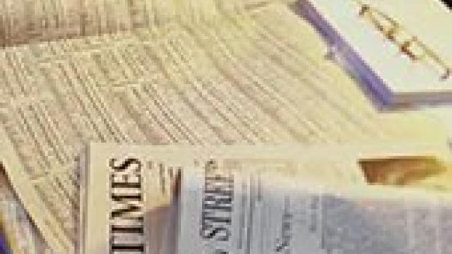 Newspapers spread out on a table with a pair of glasses and a notepad.